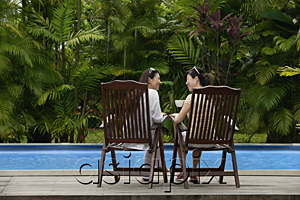 AsiaPix - Two women sitting next to swimming pool, drinking and talking