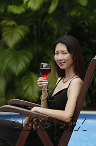 AsiaPix - Woman sitting by swimming pool, holding a glass of wine, portrait