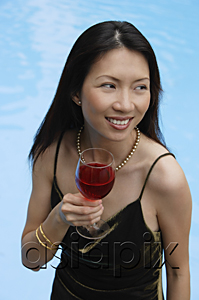 AsiaPix - Woman holding a glass of wine, looking away, swimming pool in the background