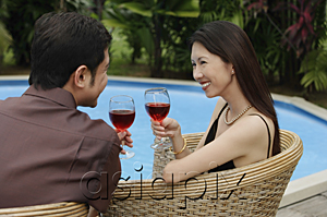 AsiaPix - Couple sitting by swimming pool, holding wine glasses