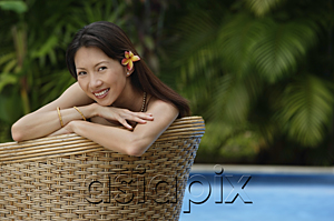 AsiaPix - Woman sitting on rattan chair, smiling at camera, wearing flower