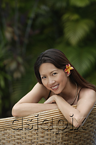 AsiaPix - Woman sitting on rattan chair, wearing flower, portrait