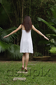 AsiaPix - Woman in garden, walking on stepping stones, hands outstretched, rear view