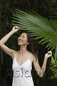 AsiaPix - Woman in white top, standing under big leaf
