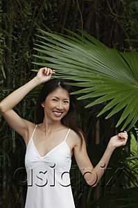 AsiaPix - Woman in white top, standing under big leaf, smiling at camera