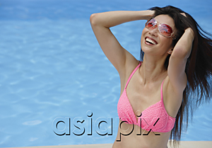 AsiaPix - Woman in pink bikini, sitting by swimming pool, hands in hair, smiling