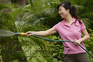 AsiaPix - Woman holding garden hose, watering plants