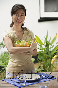 AsiaPix - Woman standing at outdoor table, holding bowl of salad