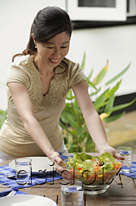 AsiaPix - Woman setting a table for a meal, putting bowl of salad on the table