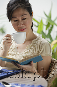 AsiaPix - Woman sipping from cup, reading a book