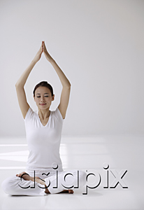 AsiaPix - Woman sitting cross legged on floor in yoga posture, with arms raised over head in prayer