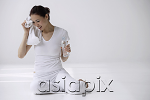 AsiaPix - Woman sitting on floor with water bottle and towel, drying off sweat on face