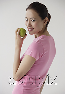 AsiaPix - Woman looking over shoulder at camera, smiling, holding apple