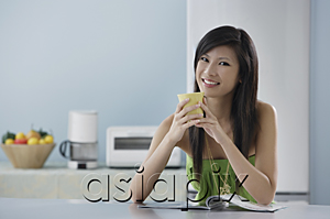 AsiaPix - woman sitting in kitchen with magazine and mug, smiling at camera