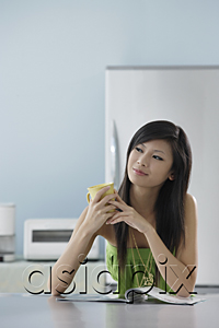 AsiaPix - woman sitting in kitchen with magazine holding mug