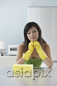 AsiaPix - woman in kitchen, looking at sponge, thinking, cleaning