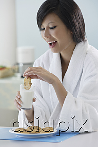 AsiaPix - woman in kitchen, dipping cooking in glass of milk, smiling