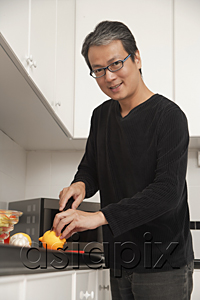 AsiaPix - Man in kitchen cutting lemon, looking at camera and smiling