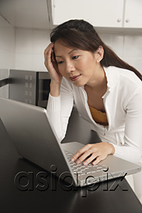 AsiaPix - Woman in kitchen leaning on counter staring at laptop / computer, with head resting on hand