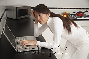 AsiaPix - Woman leaning on counter, looking at laptop / computer.