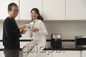 AsiaPix - Woman sitting on counter in kitchen with man standing next to her, holding coffee cups, smiling and looking at camera.