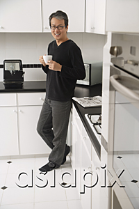 AsiaPix - Man in kitchen, leaning on counter, holding coffee cup and smiling at camera