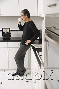 AsiaPix - Man in kitchen, leaning on counter, drinking coffee, side profile to camera.