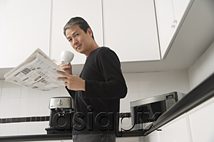 AsiaPix - Man in kitchen, holding coffee cup and newspaper and looking at camera