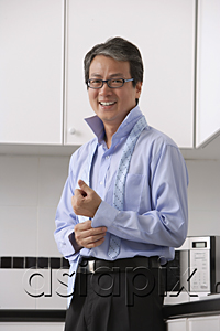 AsiaPix - Man in kitchen, buttoning his shirt and tie loose around neck.  smiling at camera.  Getting ready for work.