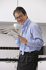 AsiaPix - Man in kitchen getting ready for work, drinking coffee and reading newspaper, smiling at camera with tie loose around neck
