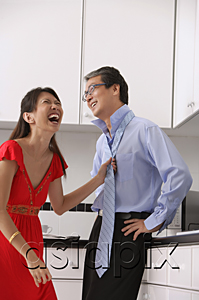 AsiaPix - Man and woman in kitchen, woman laughing and tying mans tie.  Man with hands on hip.