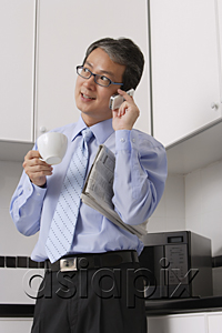 AsiaPix - Business Man in kitchen, talking on phone, holding coffee cup and newspaper, multi tasking.