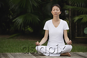 AsiaPix - Woman in tropical setting, meditating on porch, eyes closed, in yoga OM posture.