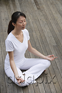 AsiaPix - Woman meditating on porch, eyes closed, in yoga OM posture.