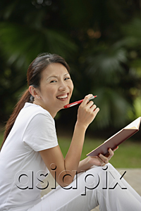 AsiaPix - woman sitting outside in tropical setting, writing in journal, diary.  looking at camera, smiling.