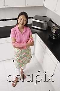 AsiaPix - woman standing in kitchen, wearing gloves and apron for cleaning.