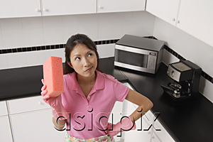 AsiaPix - woman standing in kitchen, wearing gloves and apron for cleaning, holding sponge and thinking.