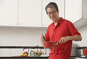 AsiaPix - Man in kitchen cooking with sauce pan, looking at camera