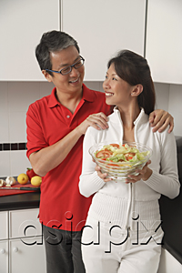 AsiaPix - Man and woman in kitchen holding salad bowl and looking at each other smiling