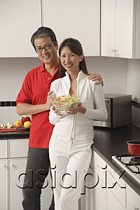 AsiaPix - Man and woman in kitchen holding salad bowl and looking at camera smiling