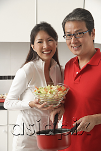 AsiaPix - Man and woman in kitchen cooking, holding salad, looking at camera, smiling