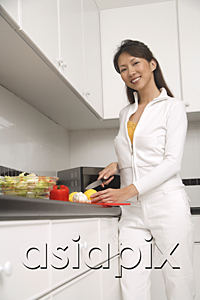 AsiaPix - woman standing in kitchen cutting vegetables and fruit, cooking, smiling at camera