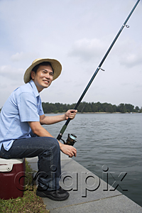 AsiaPix - Man sitting on cooler, fishing with fishing pole