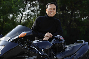 AsiaPix - Man standing by black motorcycle, smiling at camera