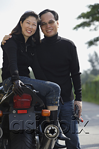AsiaPix - Mature couple looking at camera, woman sitting on motorcycle