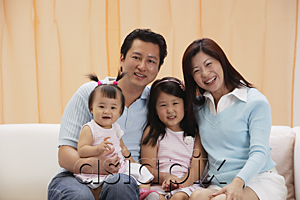AsiaPix - portrait of Family of 4, mom, dad and two daughters, sitting on couch, smiling, looking at camera