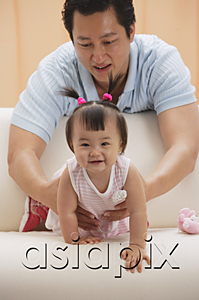 AsiaPix - father and baby girl, father holding girl as she crawls on couch