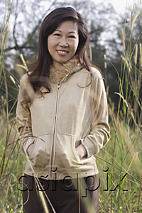 AsiaPix - Woman standing in tall grass, hands in pocket, smiling at camera, nature