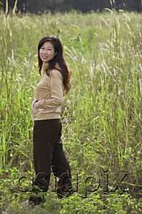 AsiaPix - Woman standing in tall grass, looking over shoulder at camera