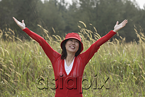 AsiaPix - Woman standing in tall grass, arms raised to sky, happy, smiling